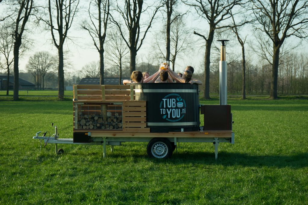 Deze afbeelding laat de mobiele hottub van Tubtoyou zien, waarbij jonge mensen proostend genieten van een comfortabel bad